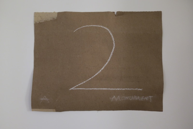 2: A Monument, 2023 — title card, chalk lettering on cardboard