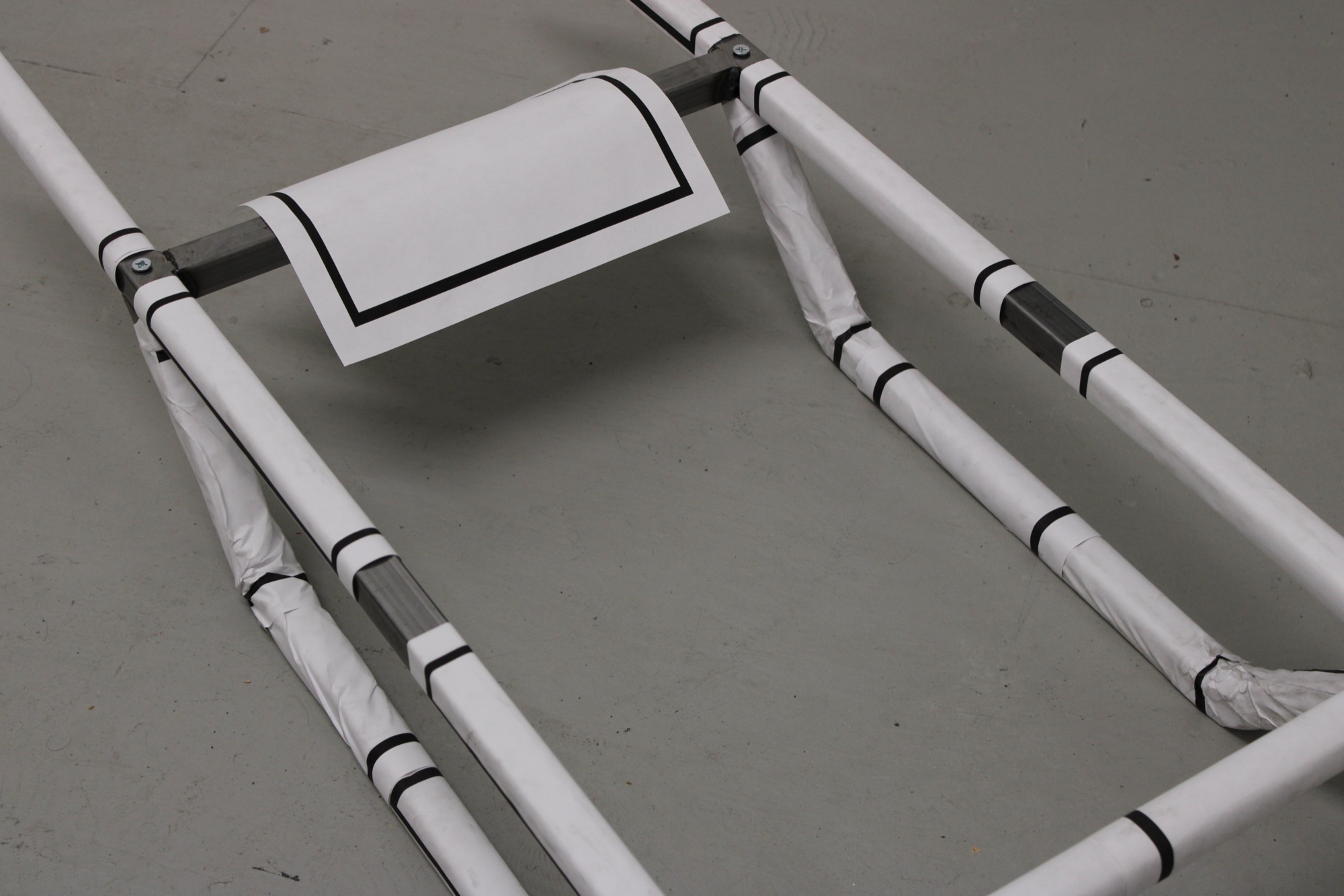 Confinement, 2026 — detail view, blank shiva notices wrapping the steel frame